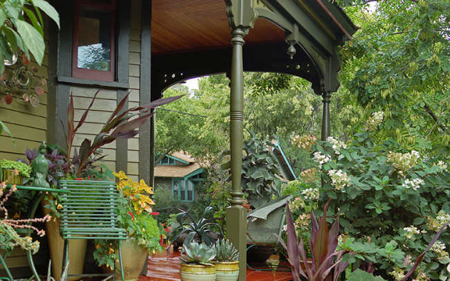 The new porch has columns that gently swell and narrow, leading up to fancy trim that harmonizes with the surrounding foliage. The lines between garden and house are further blurred by a plethora of potted plants on the porch.