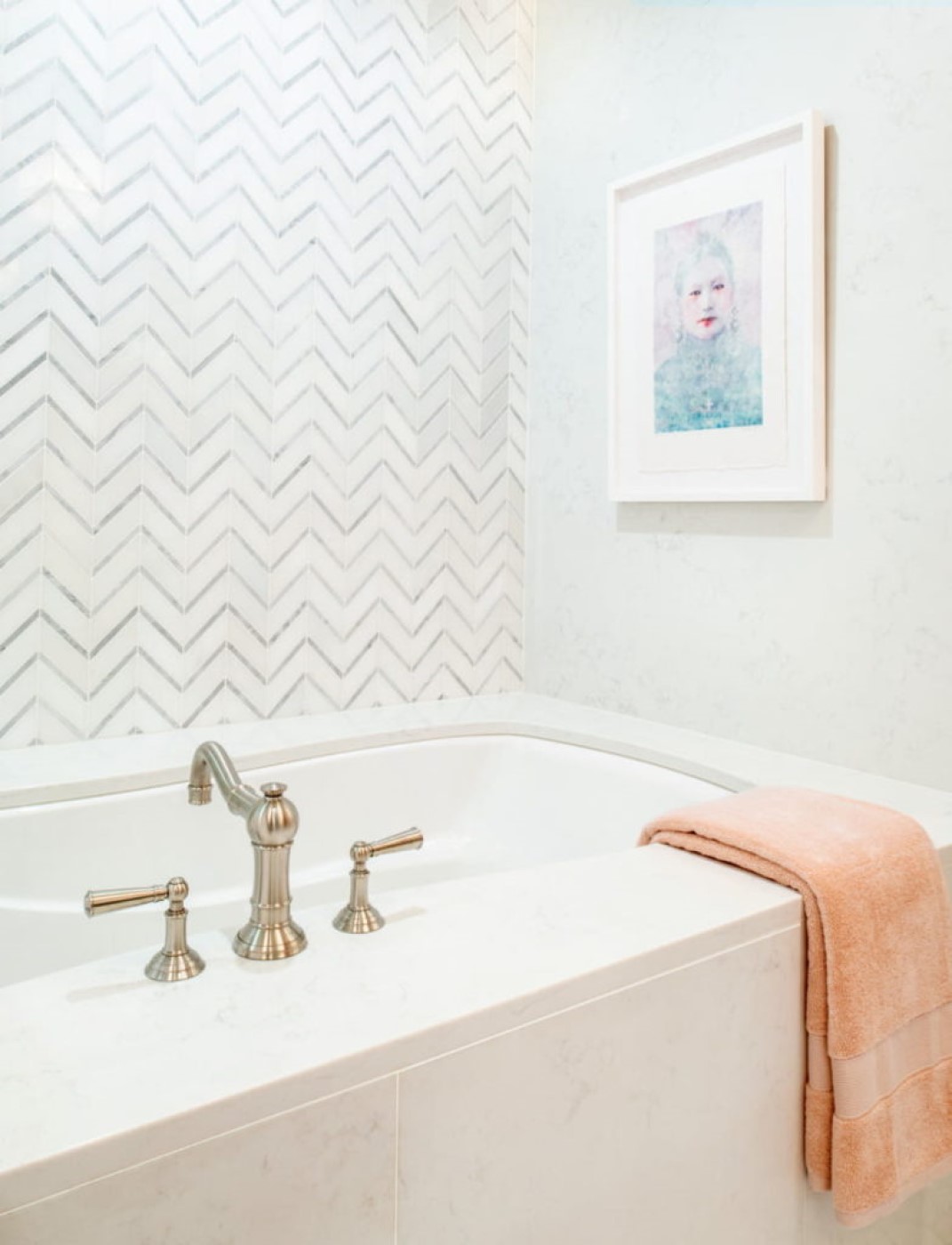 The zig zag mosaic behind the tub and shower offers a refreshing burst of ordered pattern, while the peach towels and rug add a blush of warmth.