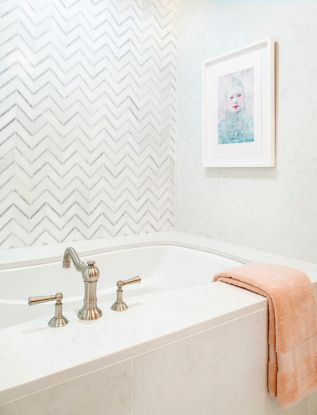 The herringbone mosaic behind the tub and shower offers a refreshing burst of ordered pattern, while the peach towels and rug add a blush of warmth.